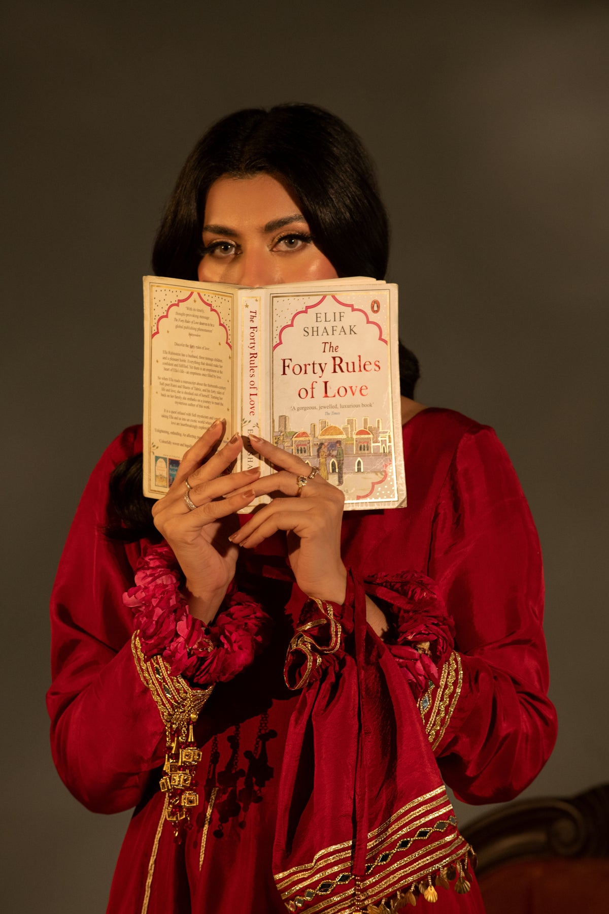 Woman in traditional attire holding a book titled 'Forty Rules of Love' by Elif Shafak against a dark background.