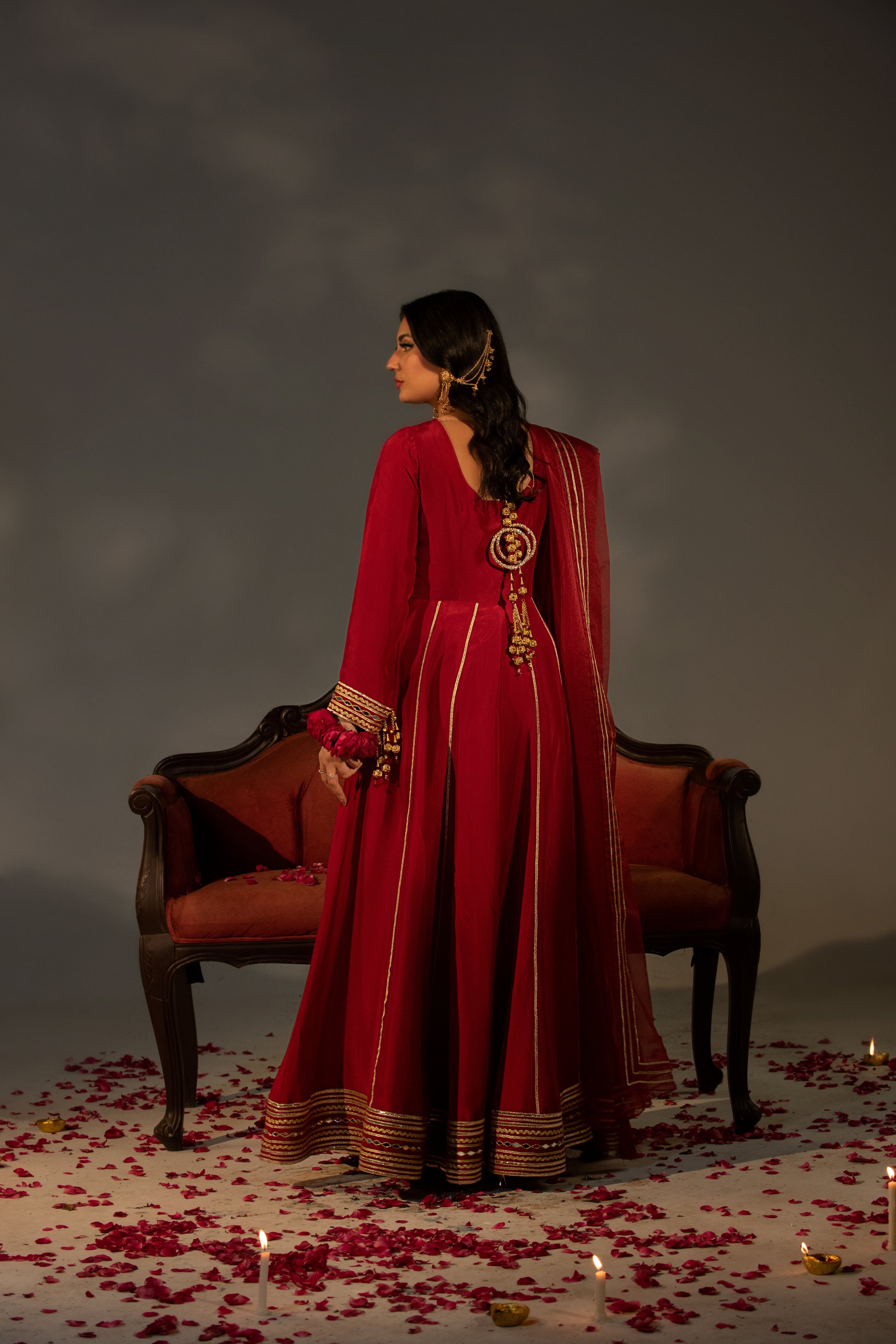 Woman in a red traditional outfit standing in a dimly lit room with candles and a chair.