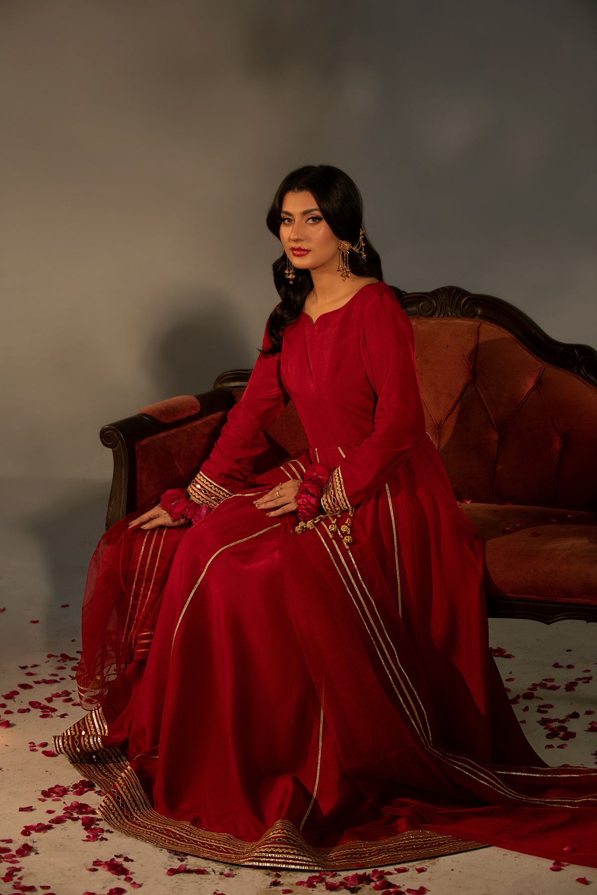 Woman in a red traditional outfit sitting on a brown couch with a gray background