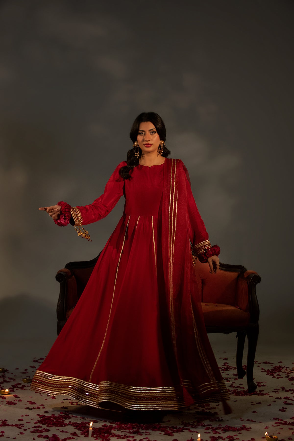 Woman in a red traditional outfit standing in a dimly lit room with a dark background.
