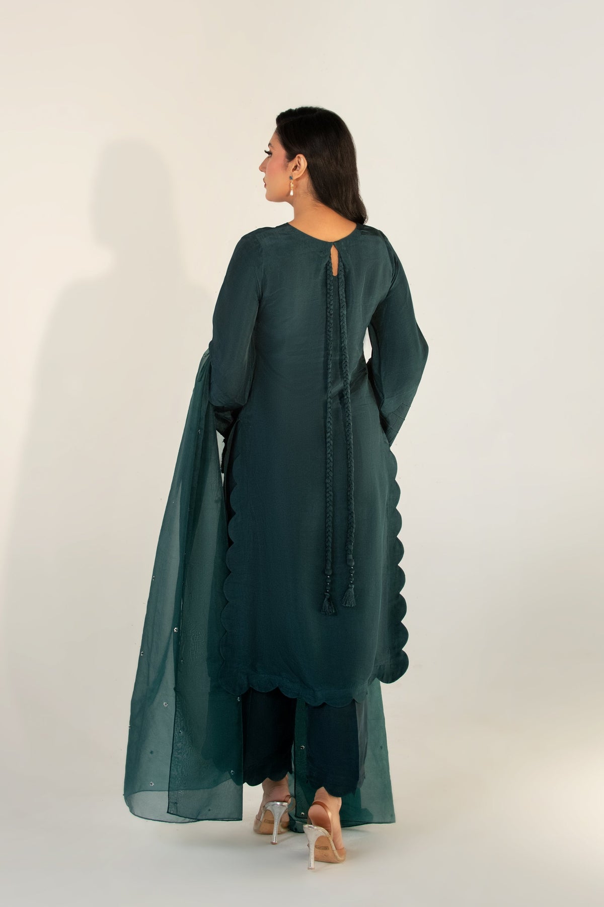 Woman wearing a teal outfit with a long jacket and pants on a white background