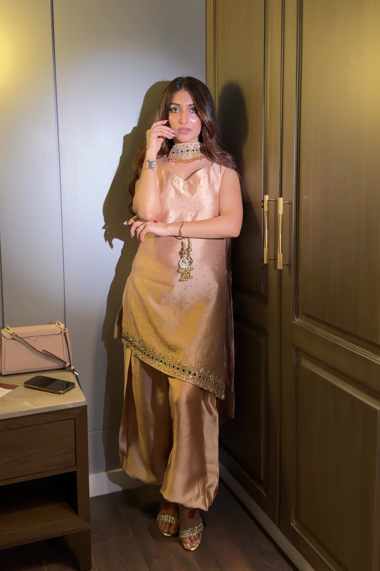 Woman in a gold dress standing in a room with a desk and wardrobe.