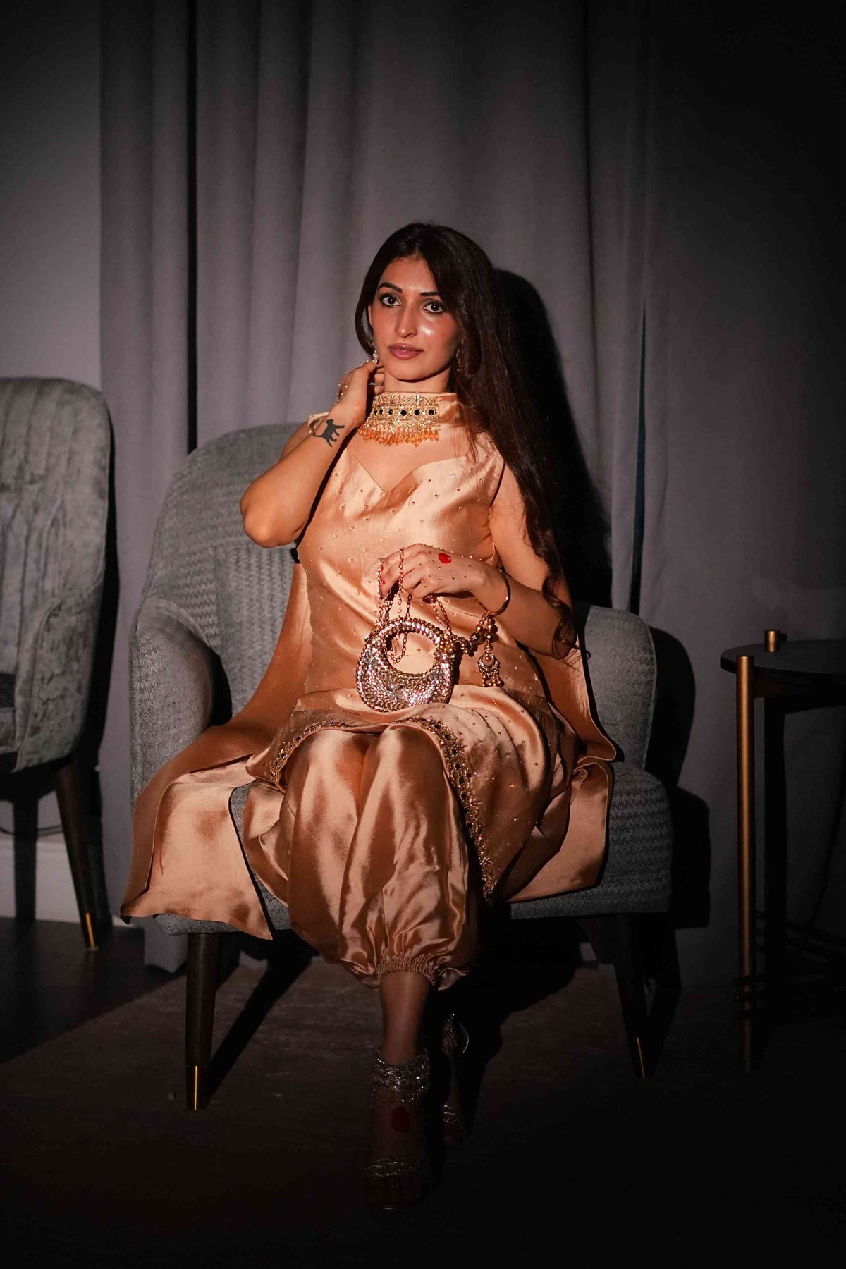 Woman in a gold dress sitting on a chair against a dark background