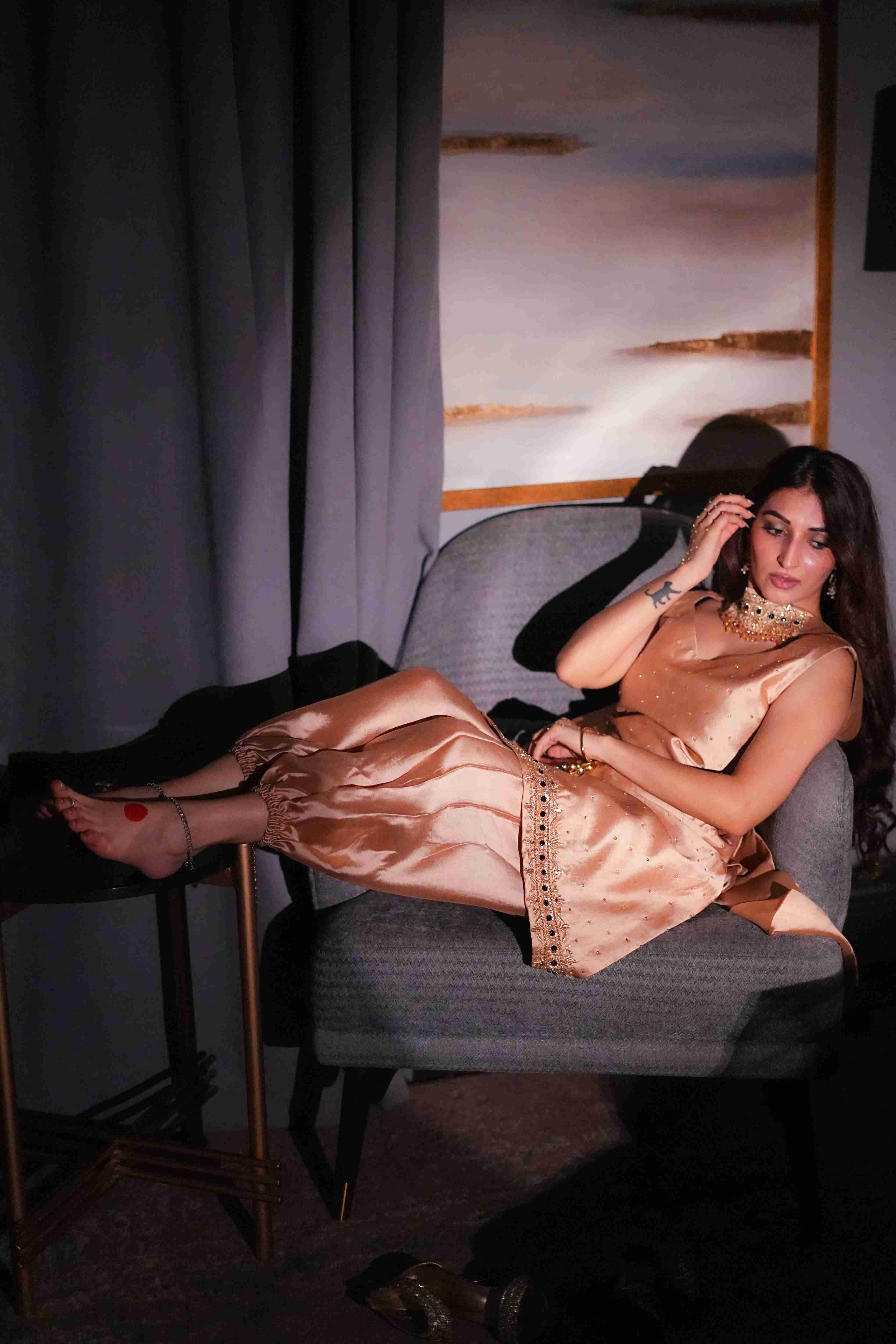 Woman in a gold dress sitting on a chair with a painting in the background