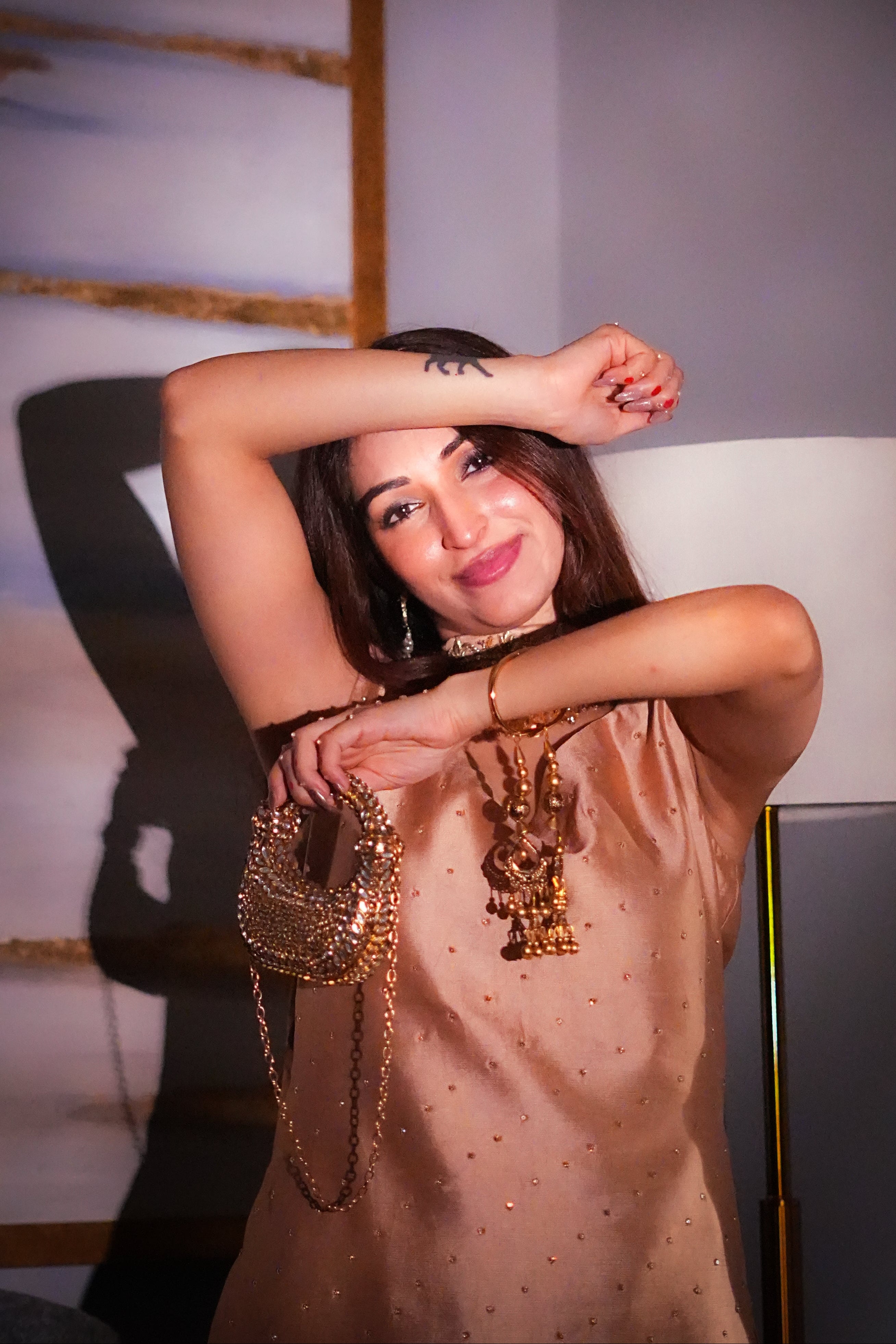 Woman posing indoors with jewelry, wearing a beige dress.