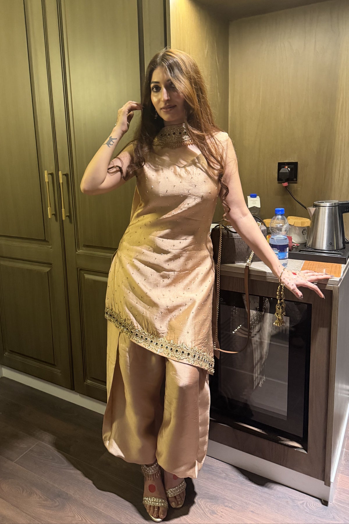 Woman in a beige traditional outfit standing in a kitchen.