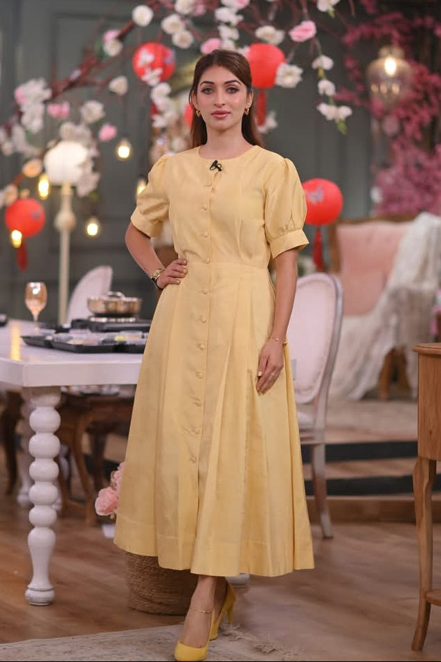 Woman in a yellow dress standing in a decorated room with flowers and balloons.