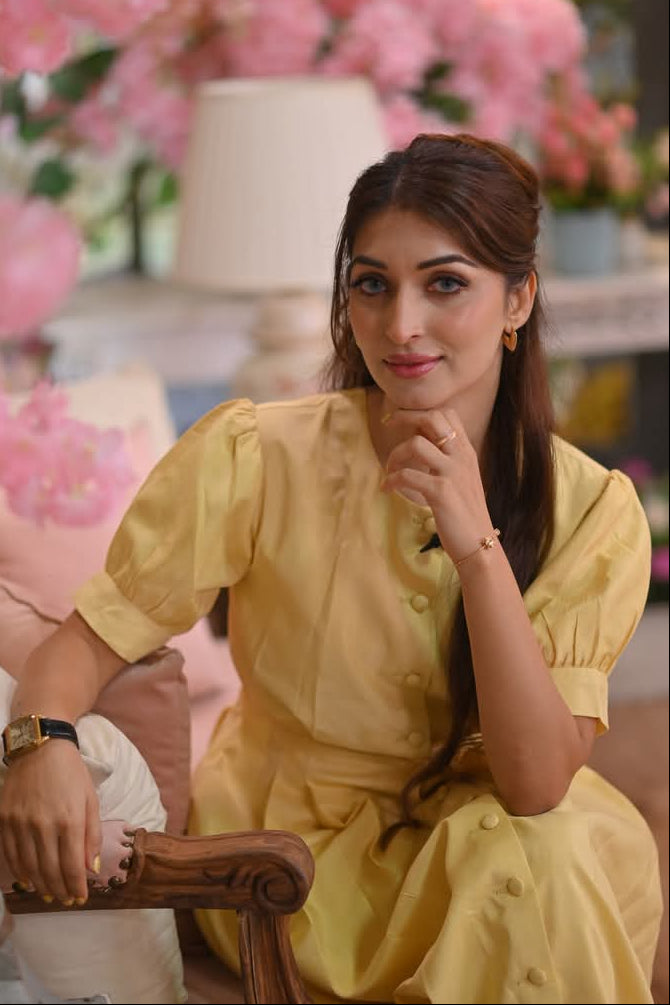 Woman in a yellow dress sitting in a decorated room with pink flowers.