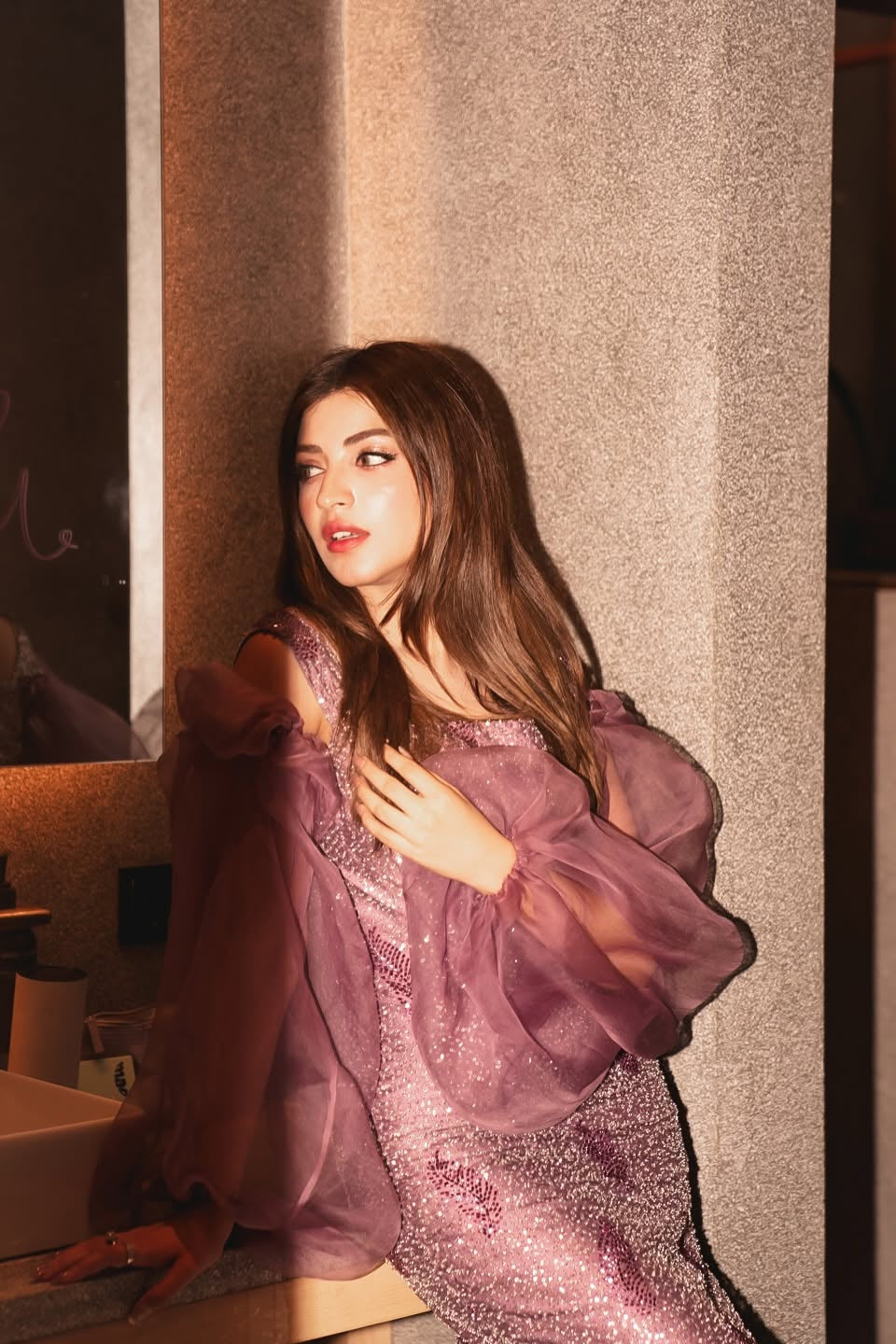 Woman wearing a purple dress with sheer sleeves in an indoor setting