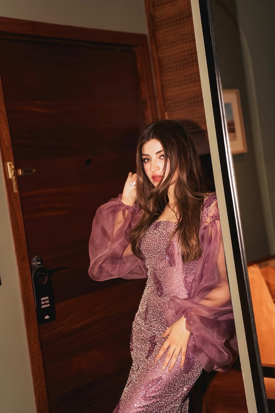 Woman in a purple dress standing in front of a mirror in a room.