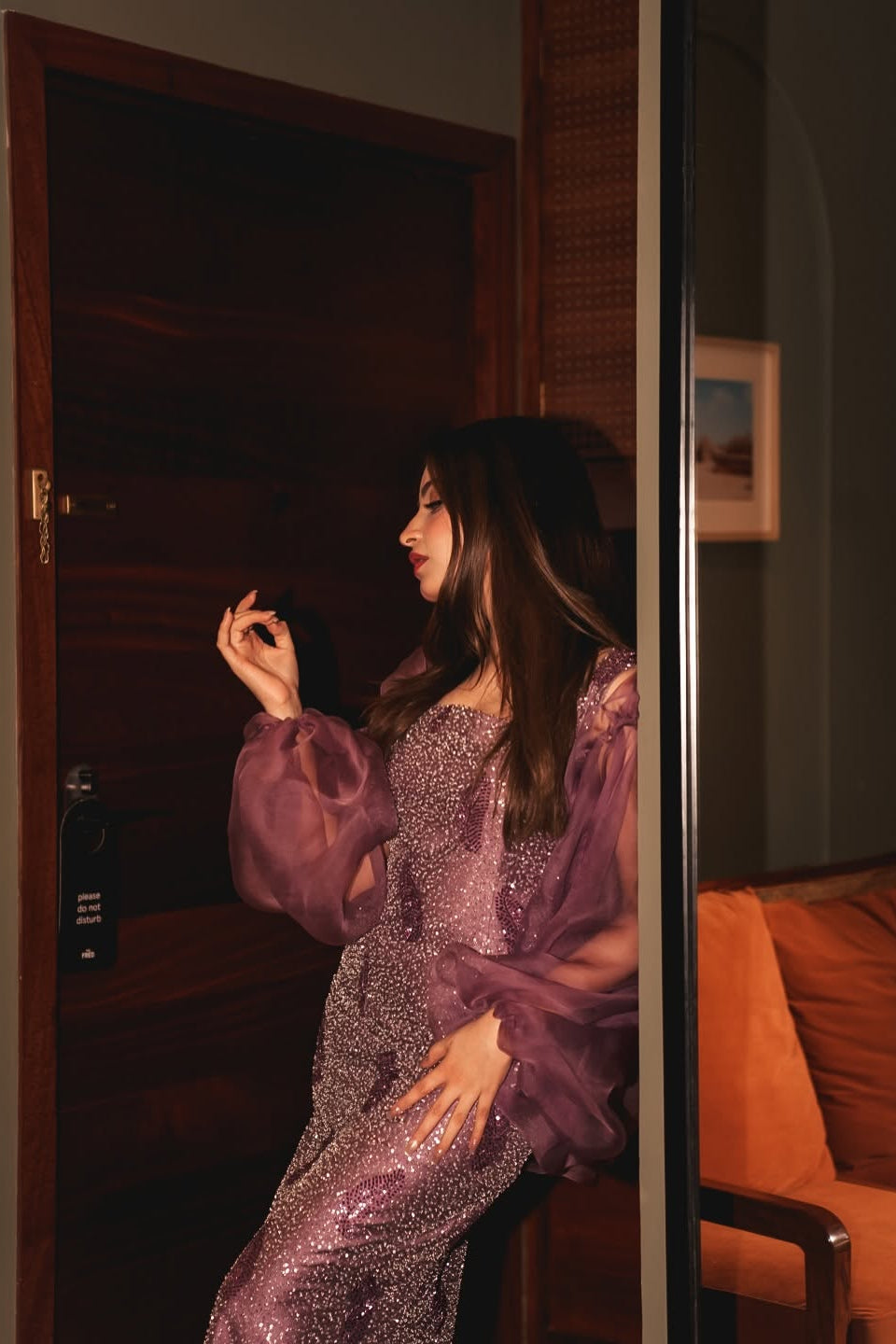 Woman in a purple dress standing in a room with an orange couch.