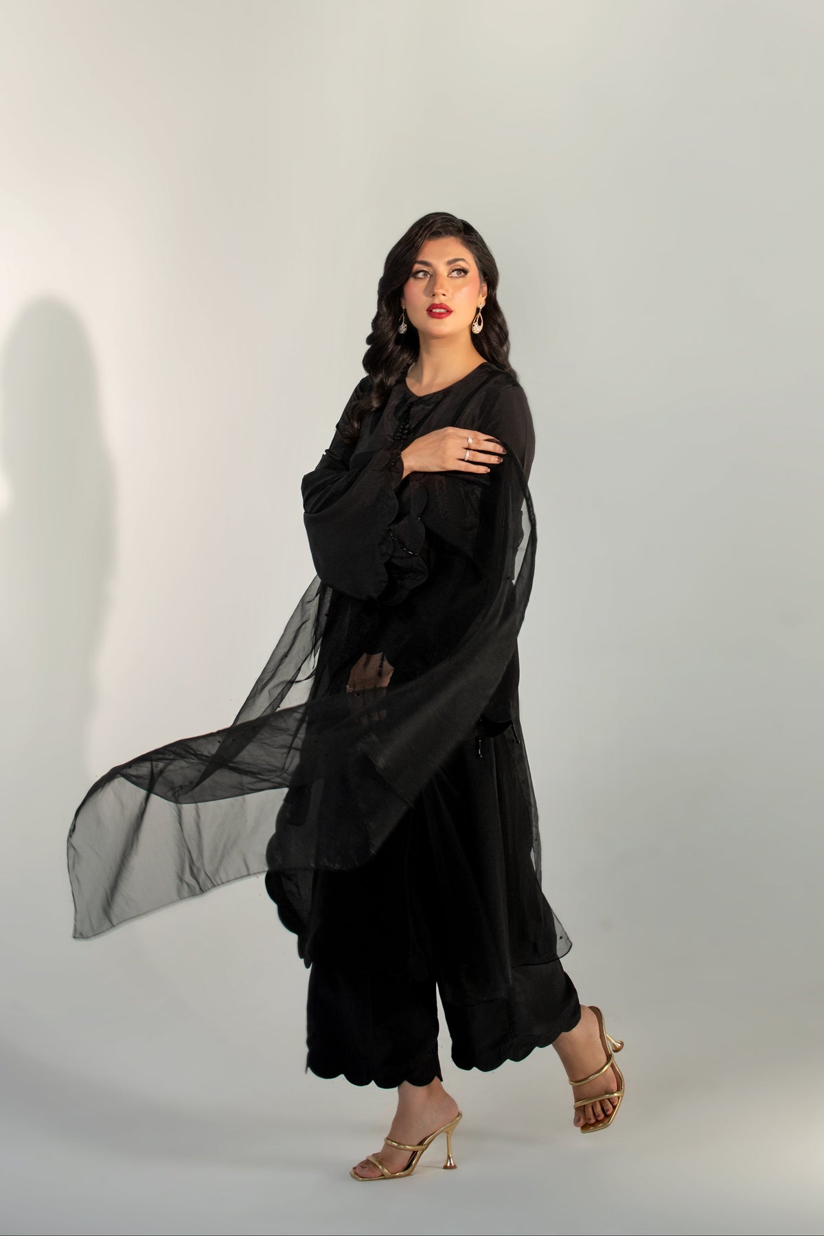 Woman wearing a black outfit with a sheer overlay against a white background