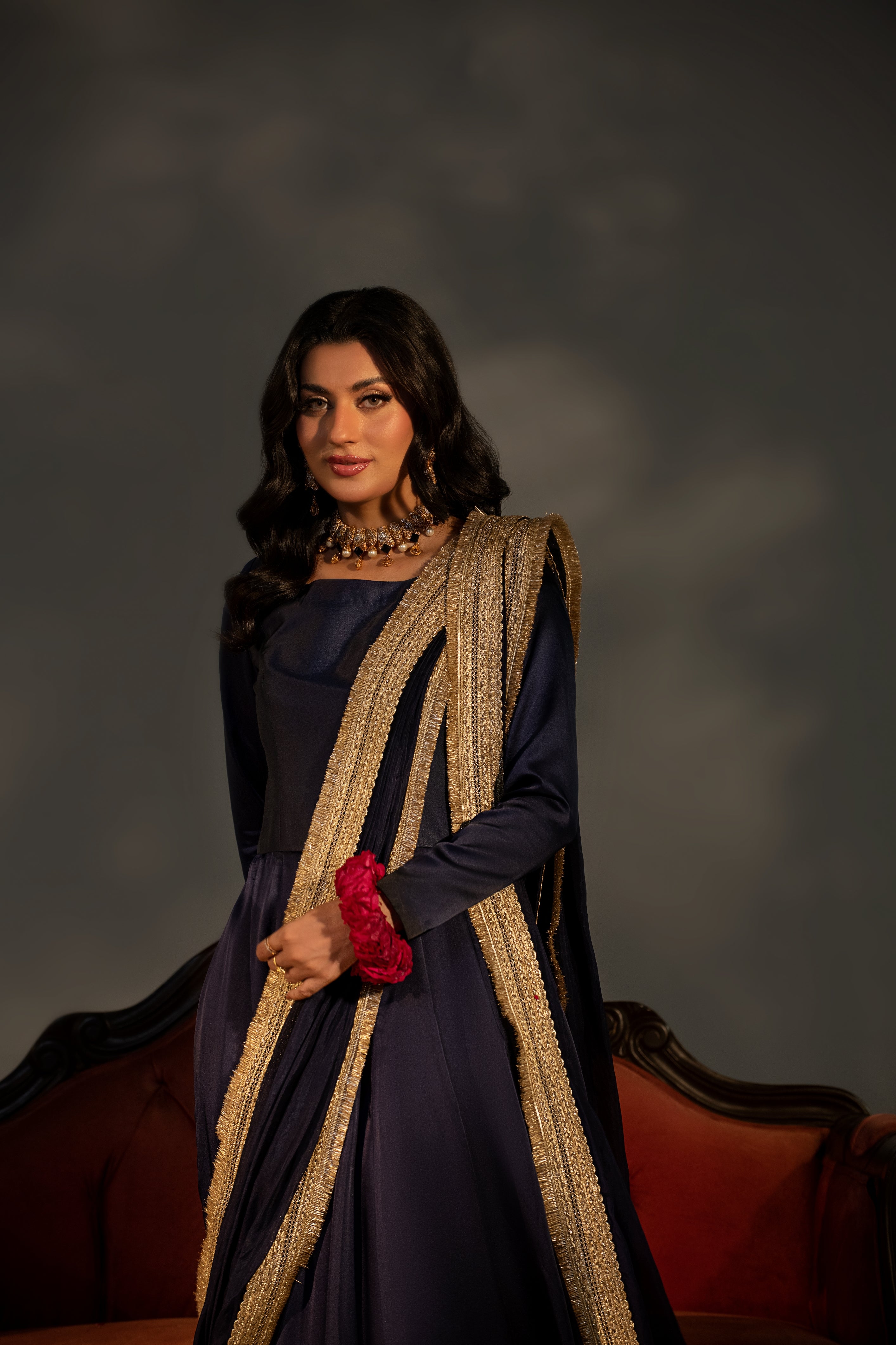 Woman in a dark blue dress with a long, decorative scarf against a dark background