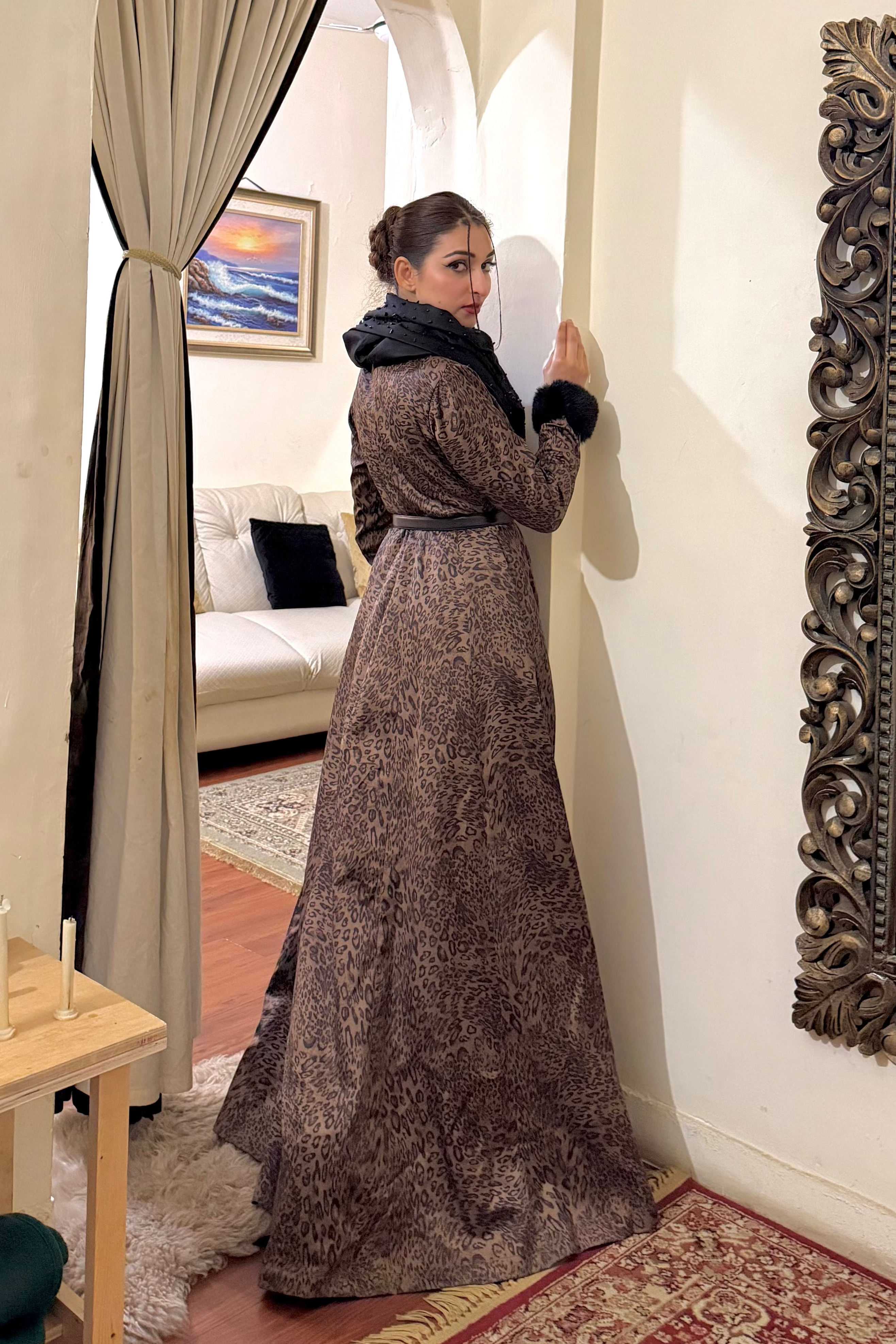Woman in a long dress standing in a room with decorative mirrors and furniture.