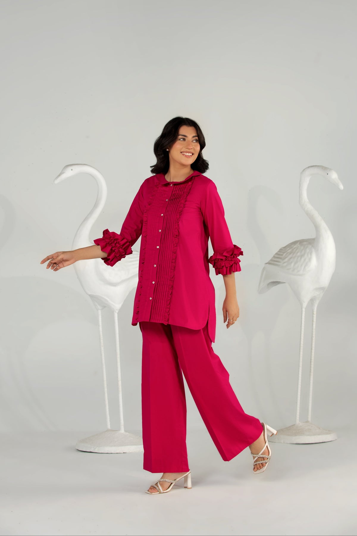 Woman in a bright pink outfit standing between two white swan-shaped chairs on a light gray background