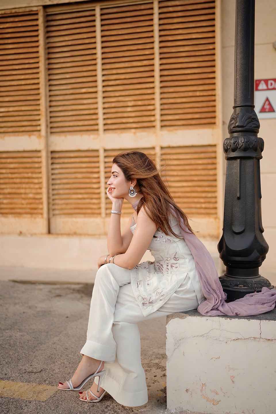 Woman sitting on a ledge by a building with wooden shutters.