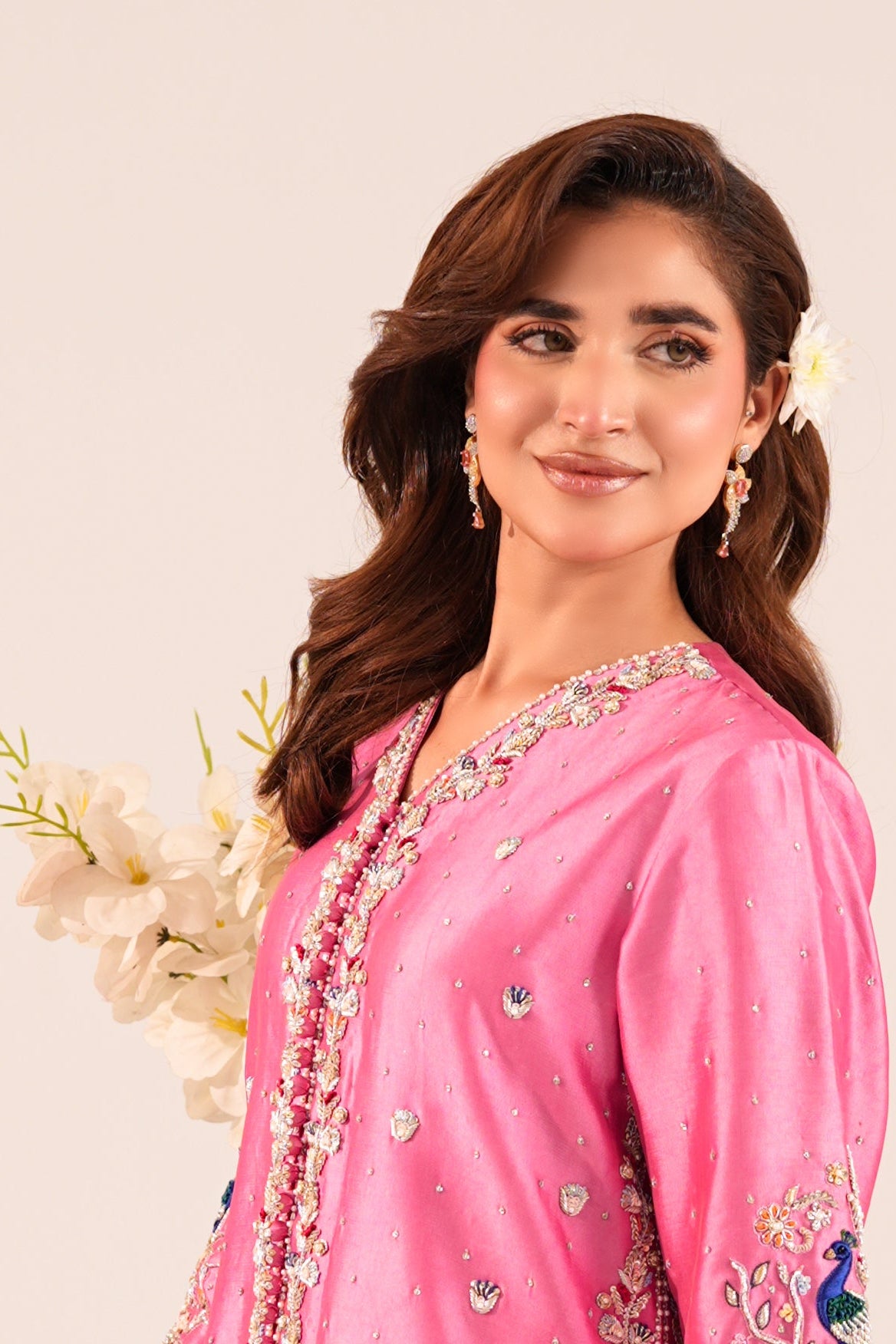 A woman modeling a pink embroidered traditional outfit against a plain light beige studio background.