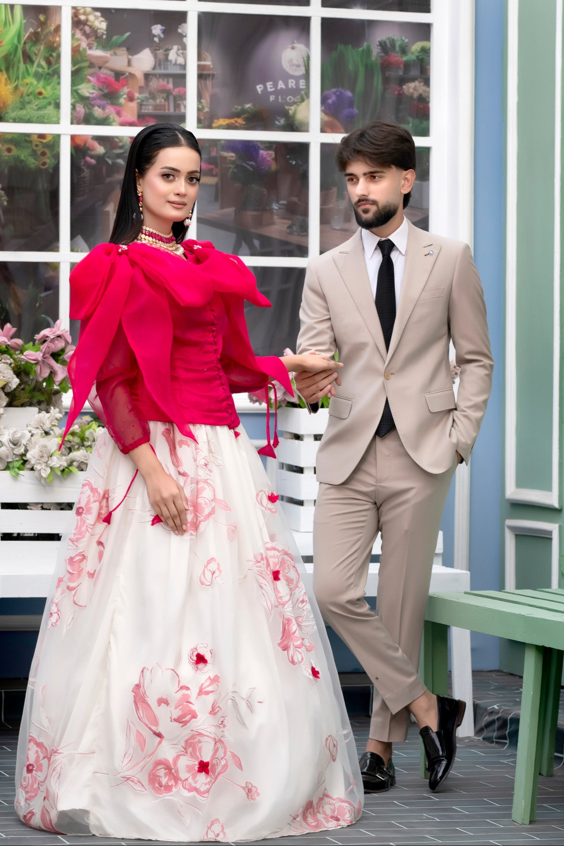 Man and woman in formal attire standing in front of a decorative window with floral patterns.