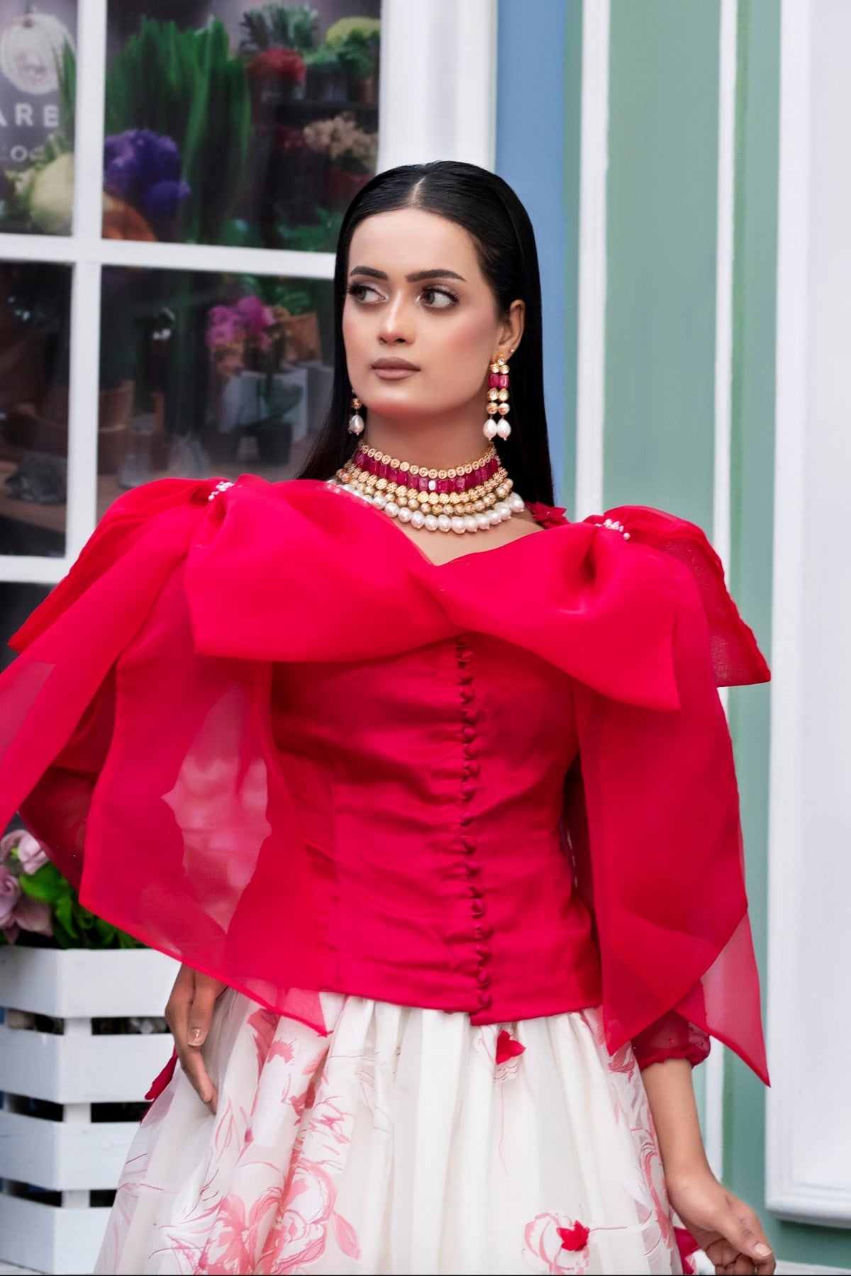 Woman in a red top and white skirt standing in front of a building with large windows.