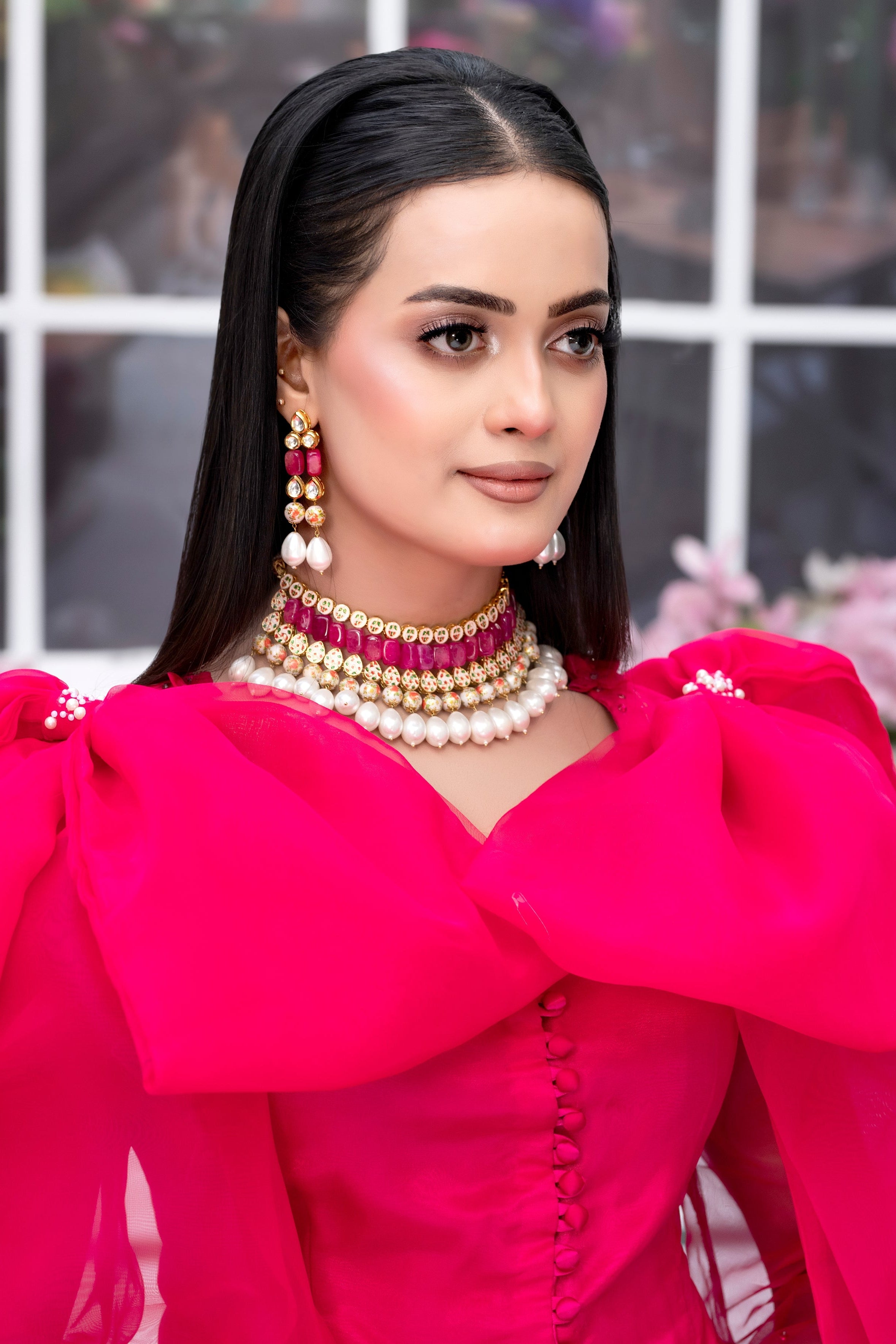 Woman wearing a bright pink outfit with large earrings and a necklace, standing indoors.