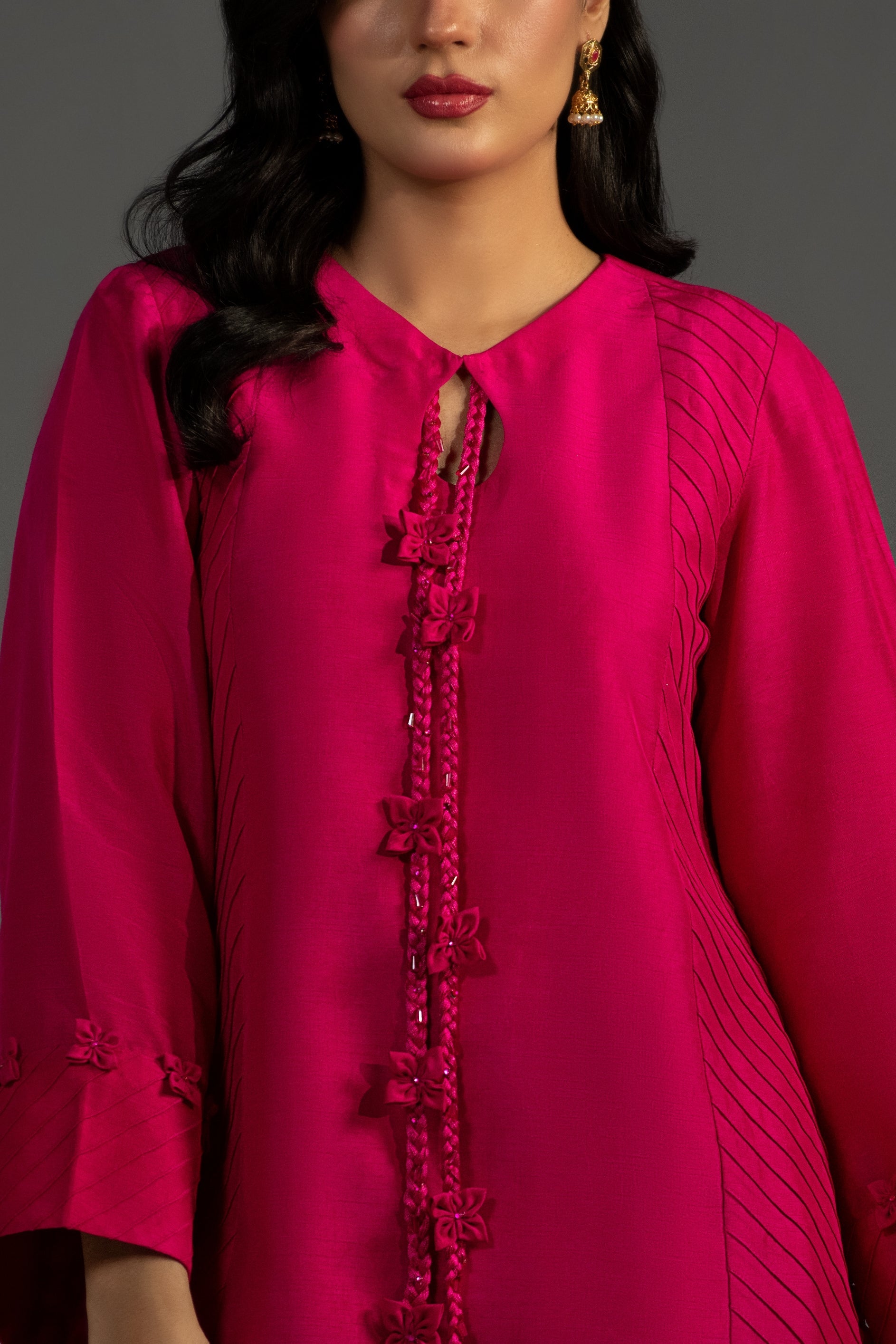 Woman wearing a bright pink traditional outfit with intricate designs on a gray background