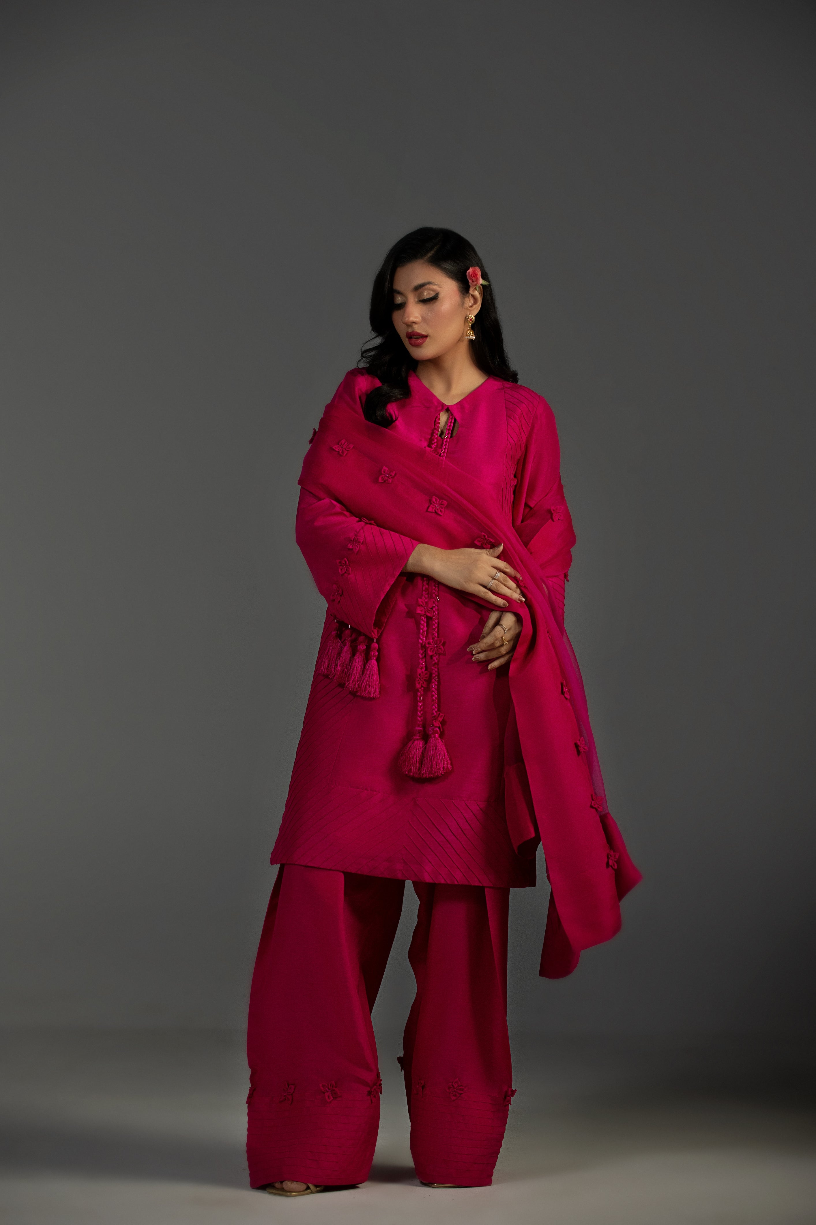 Woman wearing a bright pink traditional outfit with a shawl against a gray background