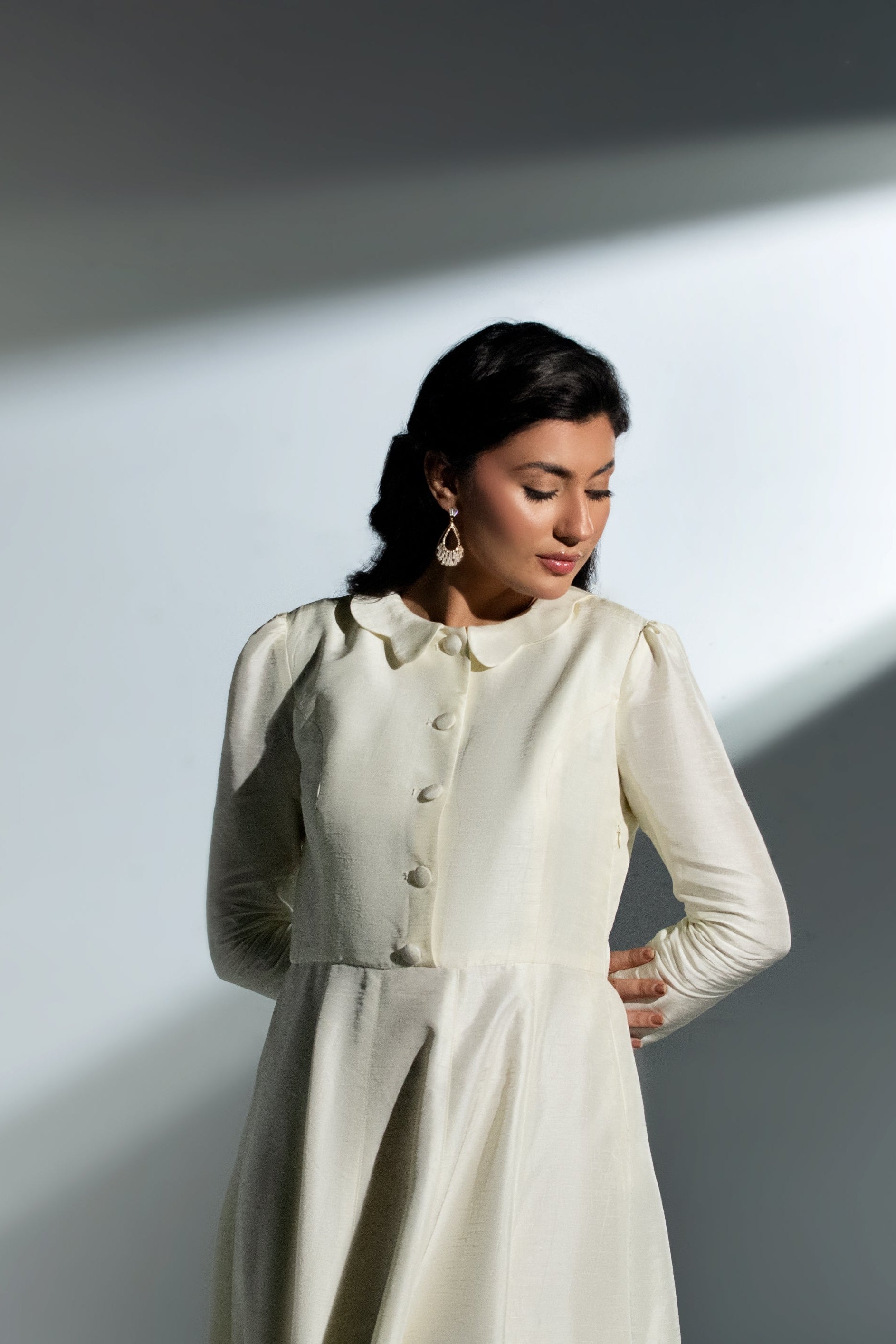 Woman wearing a white outfit with a high collar against a gray background