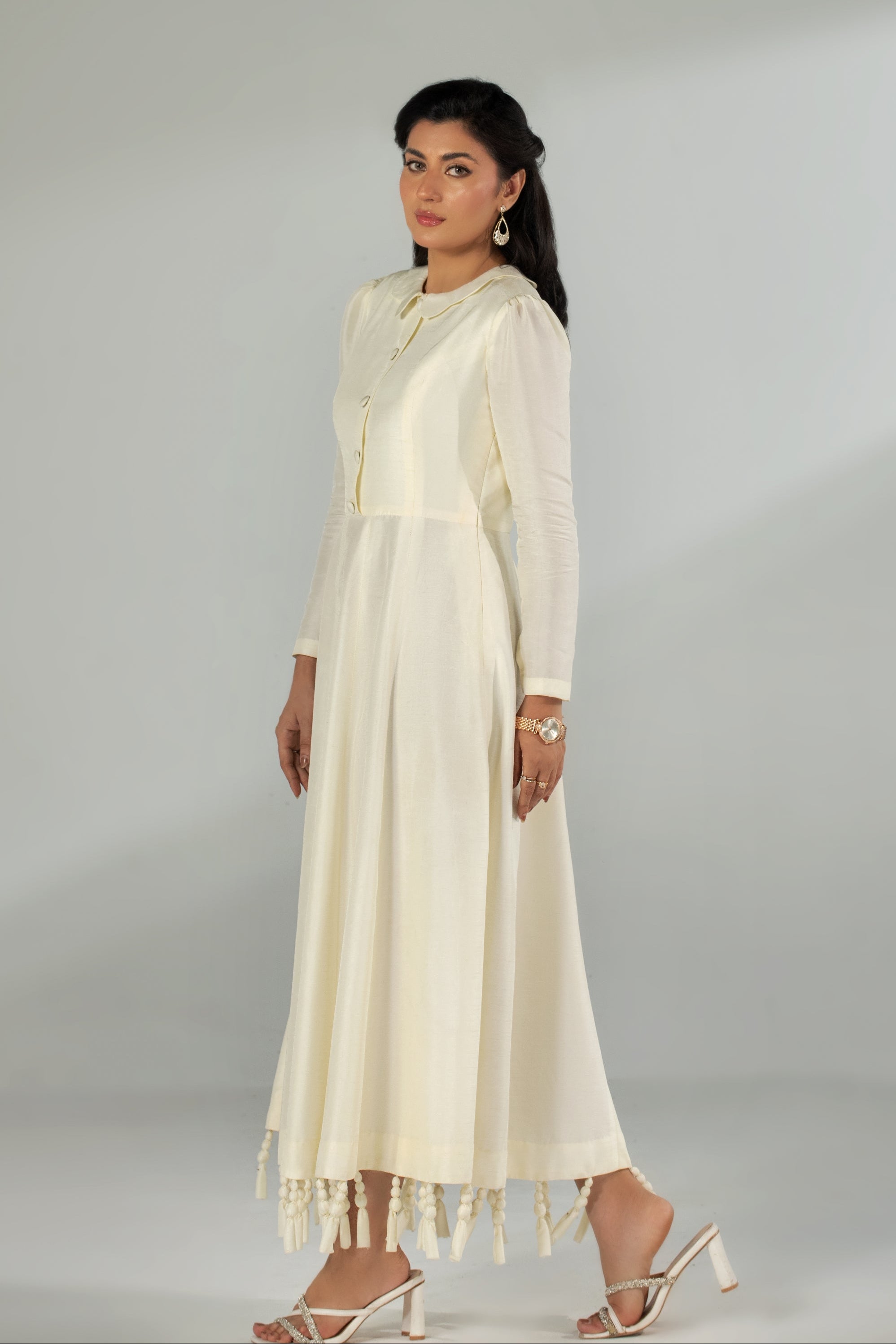 Woman wearing a long cream dress with a plain background