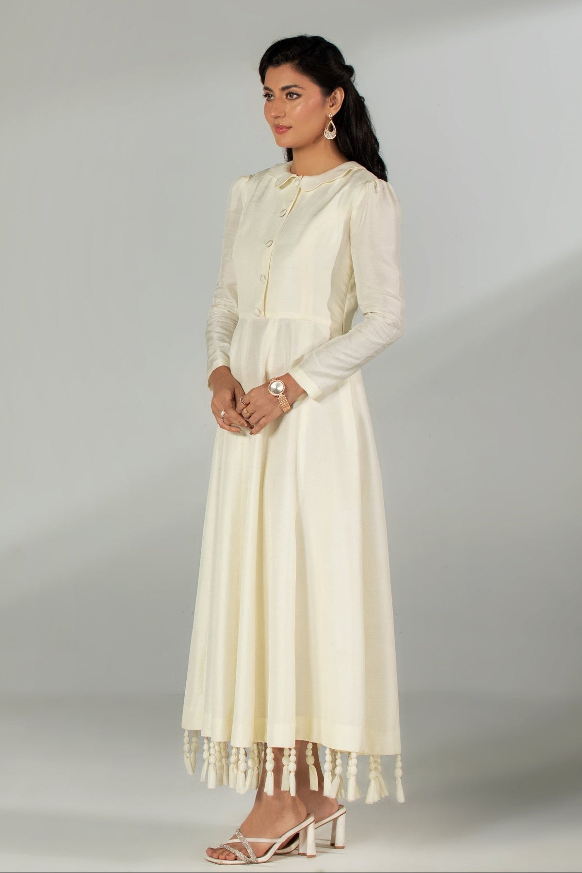 Woman wearing a long cream dress with a matching jacket against a gray background
