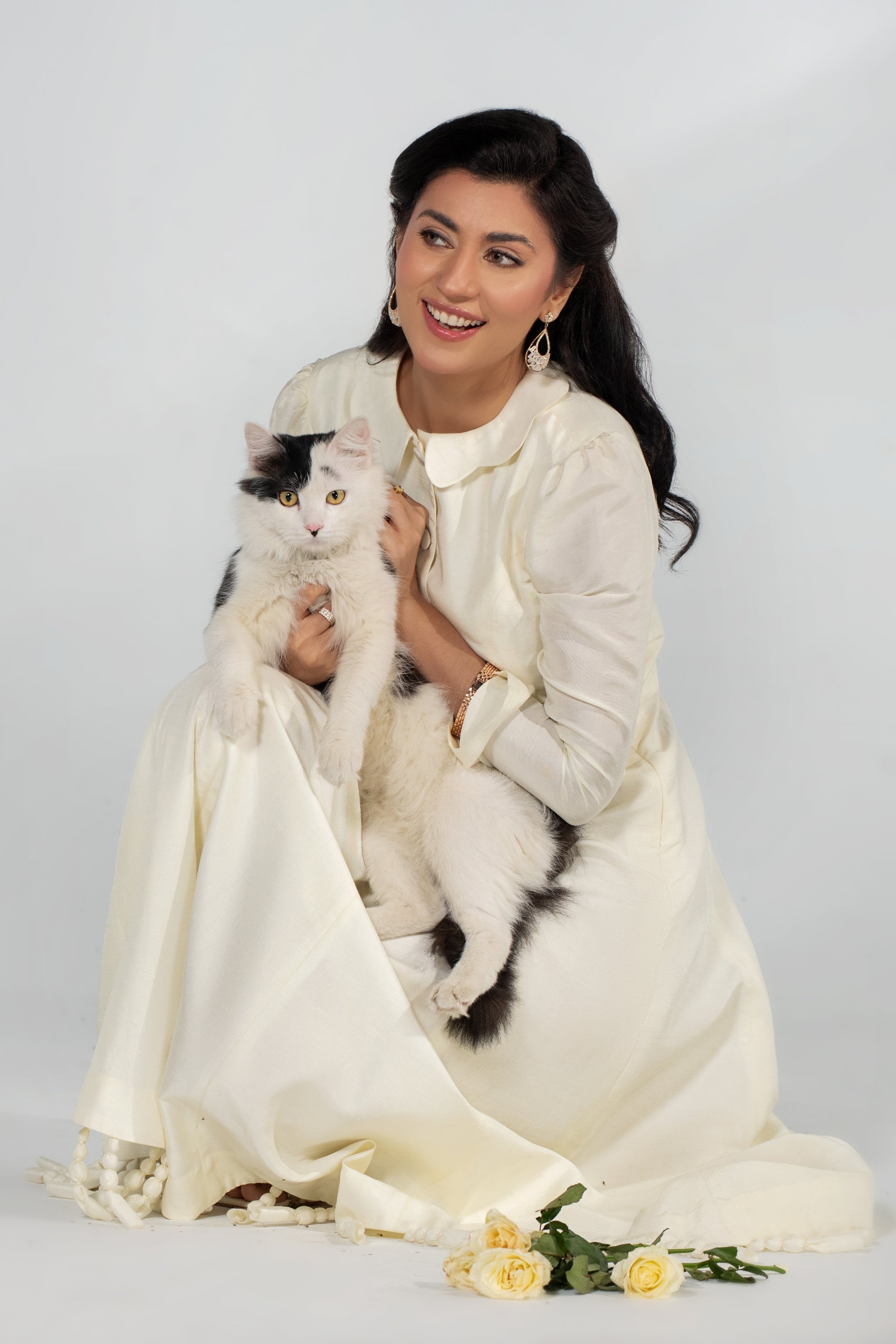 Woman in a white dress holding a black and white cat on a plain background