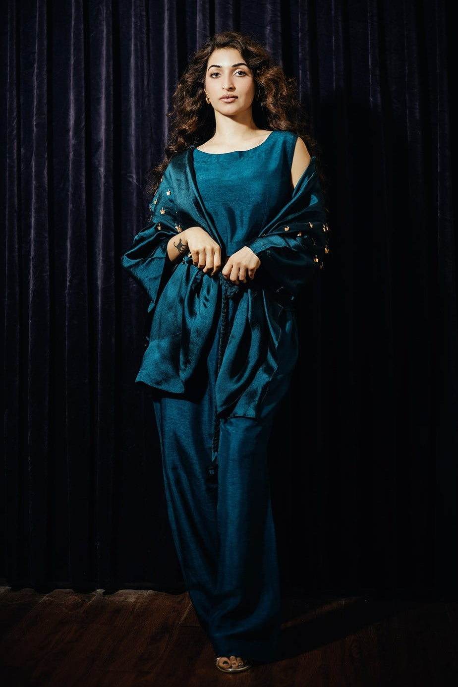 Woman in a blue outfit standing against a dark curtain