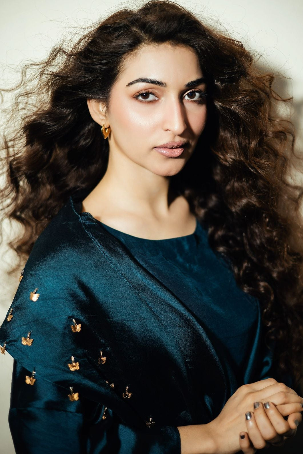 Woman wearing a dark blue top with gold details against a neutral background