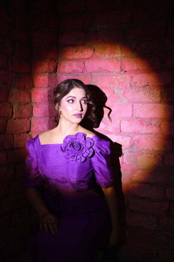 Woman in a purple dress standing against a brick wall with a spotlight effect.