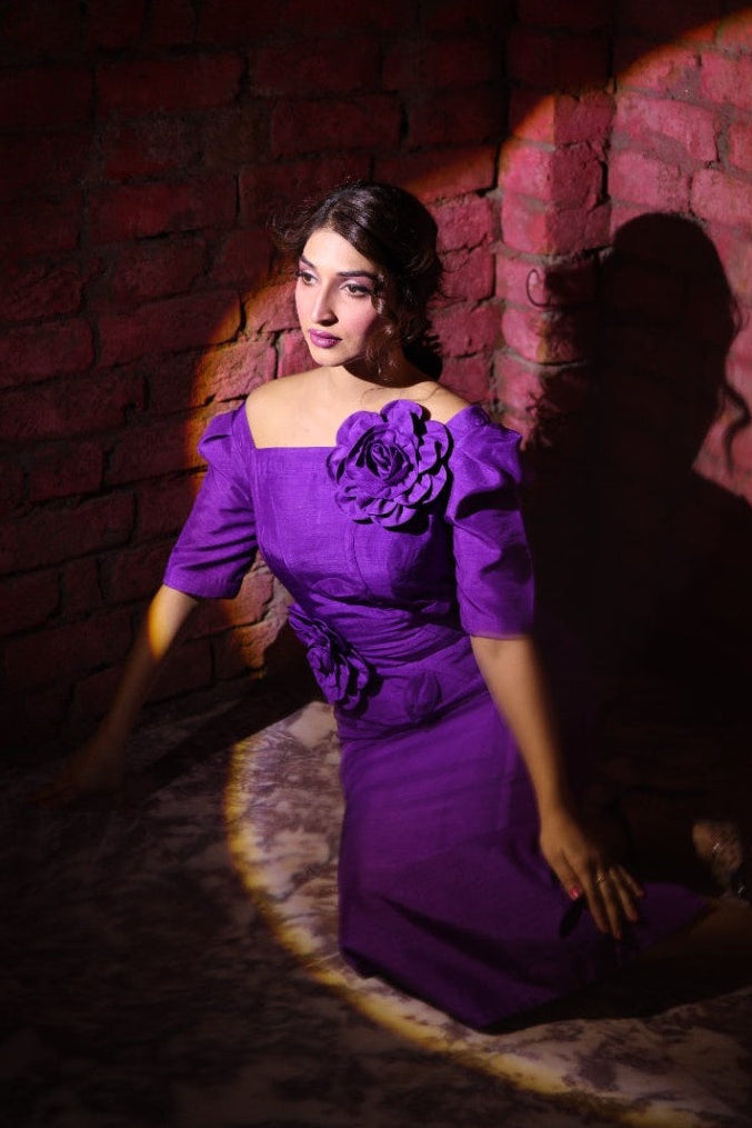 Woman in a purple dress sitting against a brick wall with dramatic lighting.