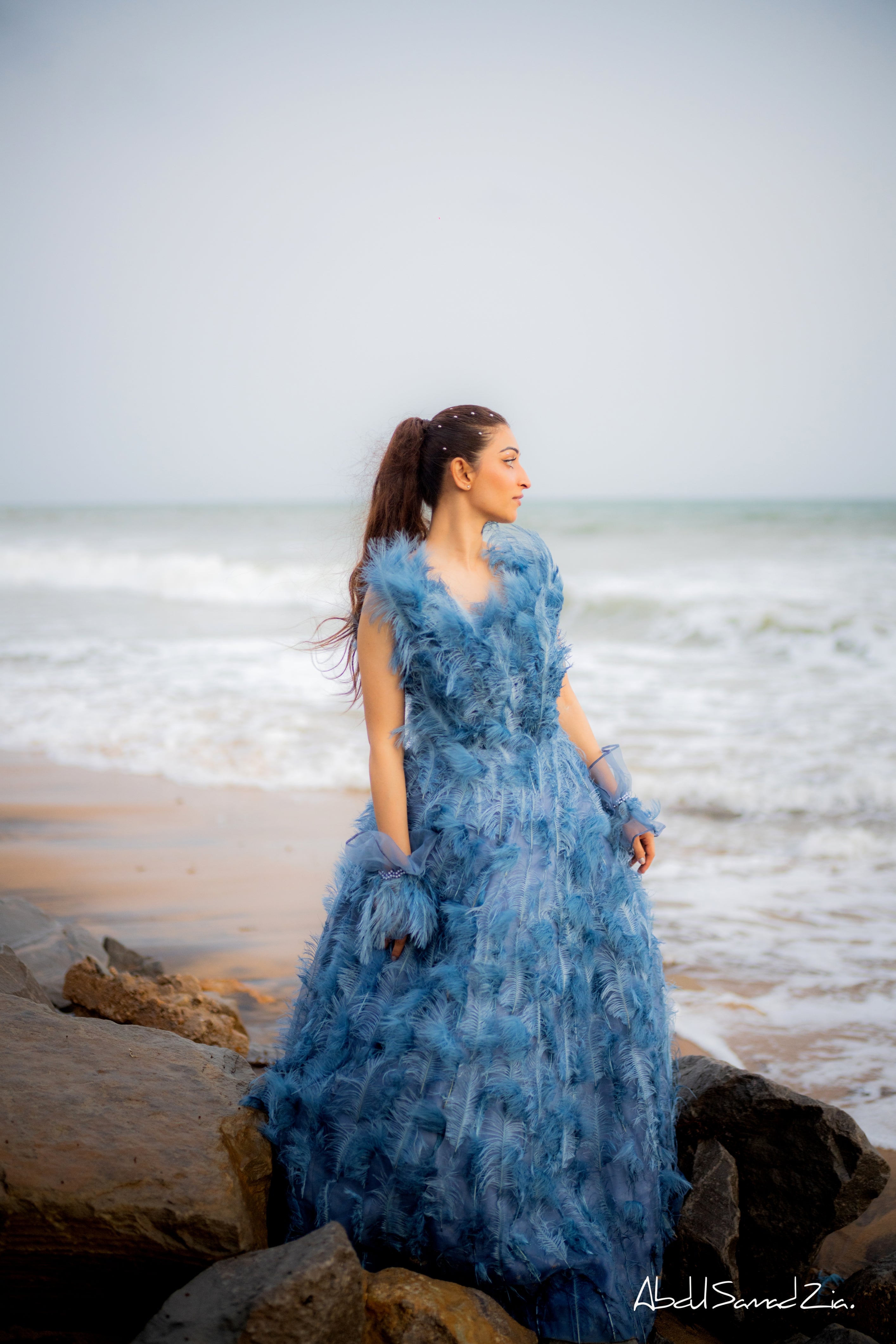 Woman in a blue dress standing on a beach with ocean waves in the background
