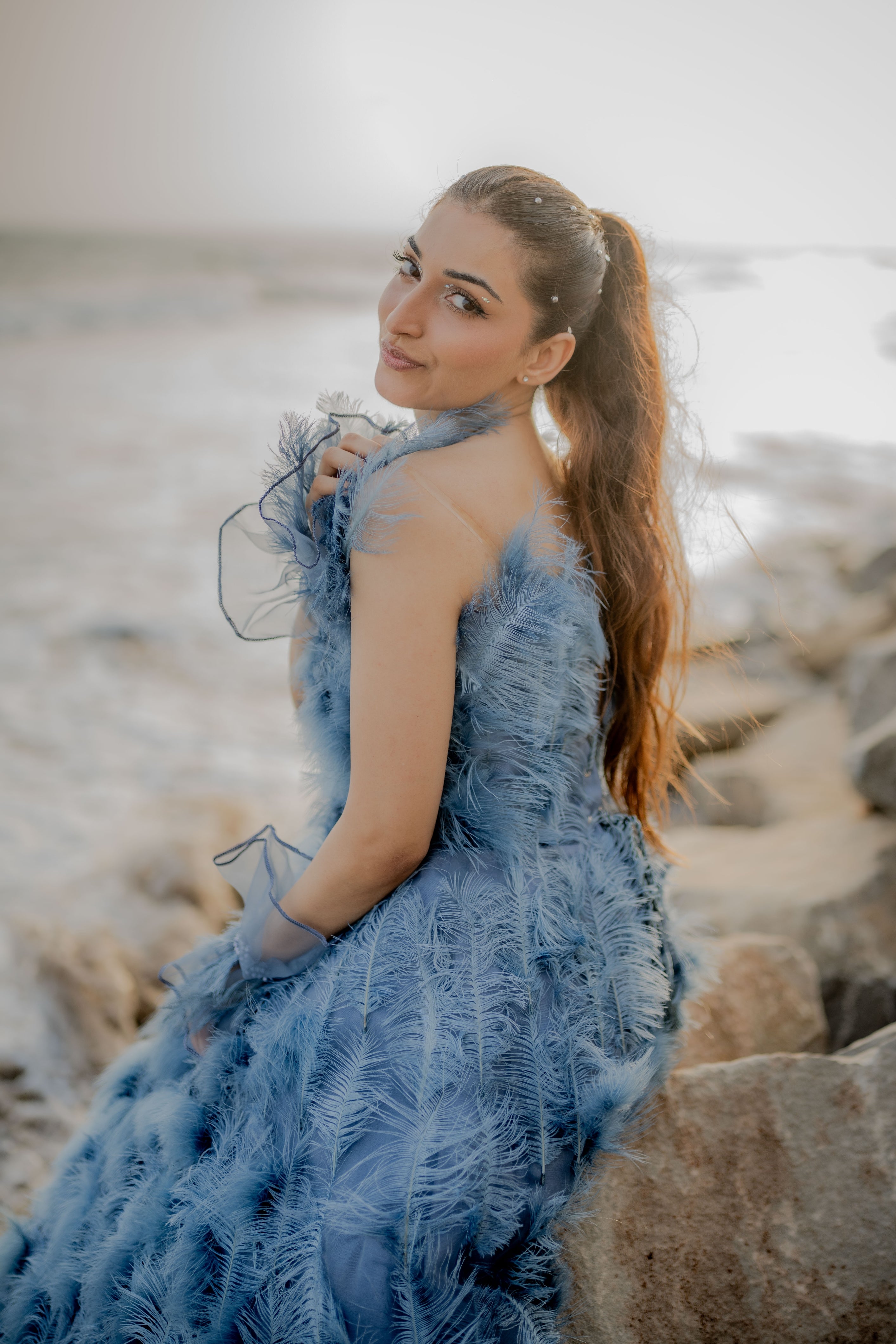 Woman in a blue feathered dress standing on rocks with a blurred background