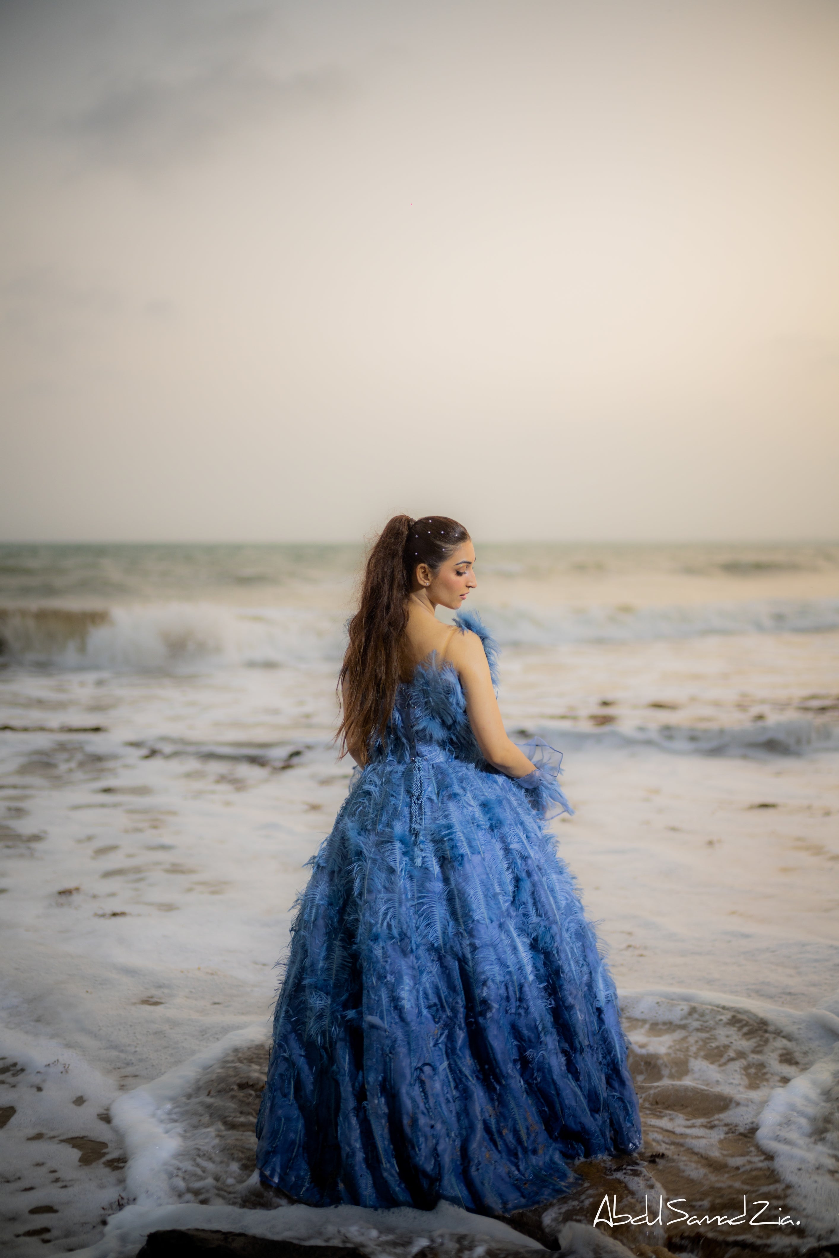 Woman in a blue dress standing on a beach with waves in the background